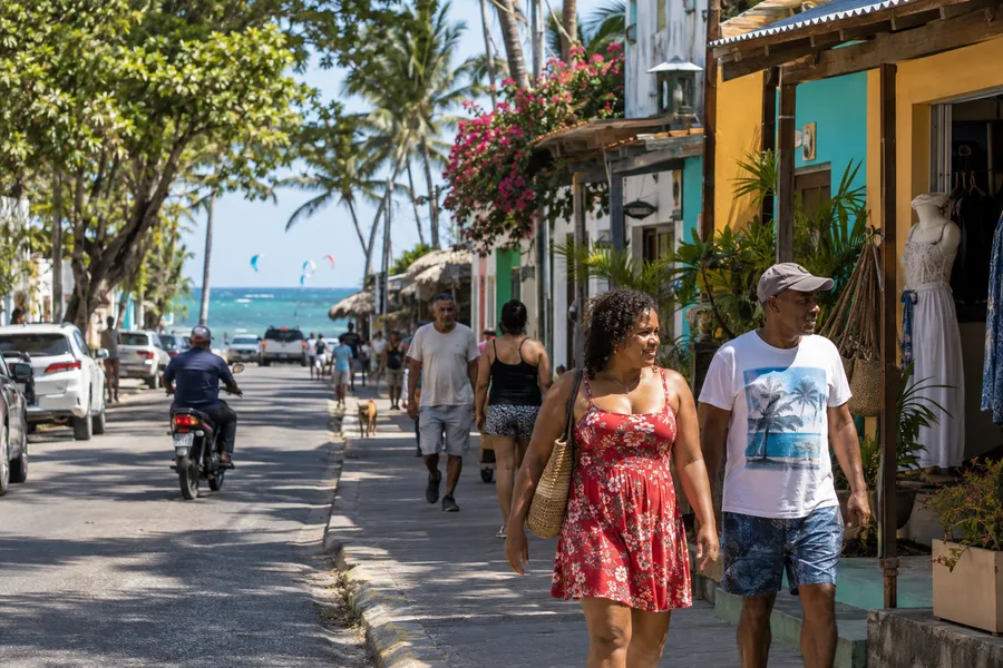 Peatones caminando de día entre comercios y árboles tropicales en Cabarete